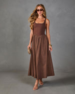 Brown midi dress with square neckline and flowy skirt, styled with strappy heels, gold accessories, and woven clutch
