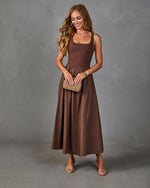 Brown sleeveless square-neck midi dress with flared skirt, worn with nude strappy heels and woven clutch