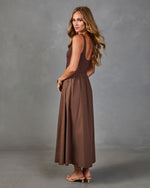 Brown sleeveless maxi dress with fitted bodice and flowy skirt, styled with nude strappy heels and gold bangles.