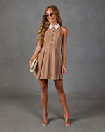 Woman wearing brown plaid tweed mini dress with white collar, gold buttons, clear heels, and cream clutch bag