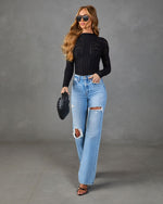 Woman wearing black long-sleeve crochet crop top, light wash ripped wide-leg jeans, black strappy heels, and black quilted clutch