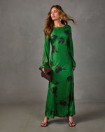 Green satin maxi dress with long sleeves and dark floral print, styled with brown woven clutch and strappy heeled sandals