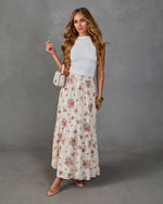Woman wearing white sleeveless crop top and cream floral maxi skirt with nude heels and beige crossbody bag