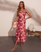 Woman wearing purple floral midi dress with bustier top, thin straps, and lace trim, styled with nude heels and cream clutch bag