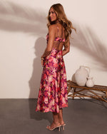 Woman wearing purple floral midi dress with open back, spaghetti straps, and pink rose print, styled with clear heeled sandals
