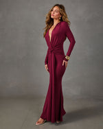 Burgundy long-sleeve maxi dress with plunging V-neckline and twist-knot waist, styled with gold bangles and clear heeled sandals