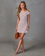 Woman wearing white and pink diagonal striped off-shoulder mini dress, holding tan woven bag, nude heels, gold accessories