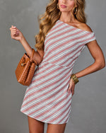Women's one-shoulder striped mini dress in rose and navy, styled with tan woven leather bucket bag and gold bangles.