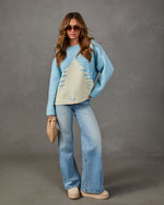 Woman in light blue oversized sweater with cream pine tree design, wide-leg light wash jeans, platform shoes and woven clutch