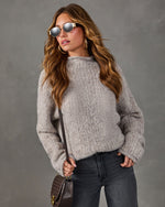 Woman in a cozy gray textured knit sweater, dark wide-leg jeans, mirrored sunglasses, gold hoops and a brown crossbody bag