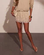 Beige lace mini skirt with scalloped hem, worn with tan blouse, gold cuff bracelets, and nude heels