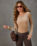 Woman in a tan velvet asymmetrical off-shoulder top, brown coated skinny jeans, aviator sunglasses and a quilted brown crossbody bag