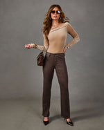 Woman in a beige velvet asymmetric neckline bodysuit, brown coated straight-leg jeans, aviator sunglasses and heeled pumps