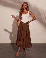 Woman wearing white lace ruffle crop top and brown polka dot tiered midi skirt with nude sandals and woven bag