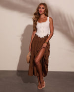 Woman wearing white lace ruffle crop top and brown polka dot maxi skirt with thigh slit, nude sandals, woven clutch