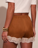Brown lace-trim mini shorts with elastic waistband, styled with white crop top and gold cuff bracelets, back view