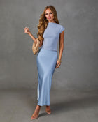 Woman wearing dusty blue cap-sleeve crop top and satin maxi skirt with nude heels and woven clutch bag
