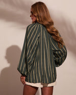 Woman wearing oversized green striped long-sleeve blouse with balloon sleeves, paired with cream shorts, back view