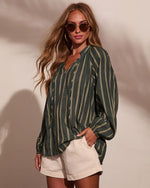 Woman wearing dark green striped long-sleeve blouse with cream shorts and gold-frame sunglasses, boho casual style