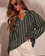 Woman wearing dark green striped linen V-neck blouse with tie detail and cream pants, styled with gold aviator sunglasses