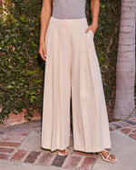 Cream wide-leg pleated trousers with high waist and side pockets, styled with white strappy sandals outdoors