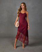 A woman models a burgundy satin slip dress with matching lace panels and sheer lace hem, styled with clear high-heeled sandals against a textured gray studio background.