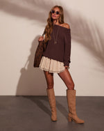 Woman in brown off-shoulder knit sweater, cream lace mini skirt, tan knee-high boots, carrying floral tote bag