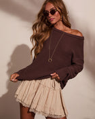 Woman wearing dark brown off-shoulder knit sweater with beige lace-trim mini skirt, gold jewelry, and oval sunglasses