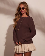 Woman wearing dark brown knit oversized sweater with cream ruffled lace-trim mini skirt, gold jewelry, and tinted sunglasses