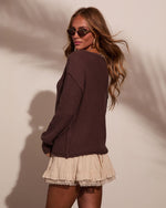 Woman wearing dark brown chunky knit sweater and cream ruffled lace-trim mini skirt, looking over shoulder, boho style