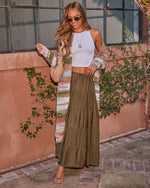 Woman wearing olive green tiered maxi skirt, white crop top, striped boho cardigan, and tan sandals outdoors