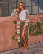 Woman in boho striped knit maxi cardigan, white crop top, olive maxi skirt with slit, and platform sandals