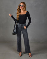 Woman wearing black lace-trim long-sleeve bodysuit, gray wide-leg raw-hem jeans, black strappy heels, woven tote bag, and sunglasses