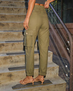 Woman wearing olive green cargo pants with button pocket and elastic cuffs, paired with nude kitten heel sandals, standing on concrete steps