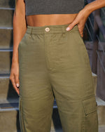 Olive green linen cargo pants with elastic waistband, wooden button, and side pockets on woman
